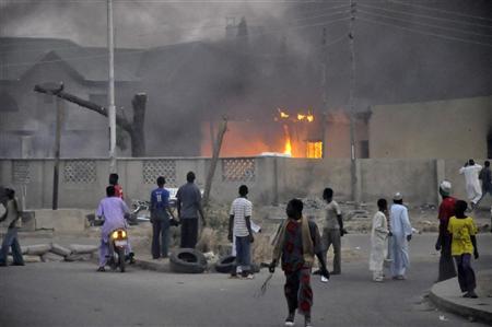 People watch as smoke rises from the police headquarters after it was hit by a blast in Nigeria's northern city of Kano