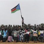 A man holds up South Sudan's new flag as South Sudanese children rehearse a dance routine ahead of a soccer match between South Sudan and Kenya as part of the independence day celebrations, July 7, 2011. REUTERS/Paul Banks/UNMIS/Handout