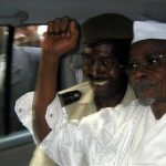 Former Chad President Hissene Habre (R) raises his fist in the air as he leaves a court in Dakar escorted by a Senegalese policeman November 25, 2005. REUTERS/Aliou Mbaye