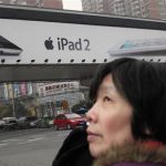 A woman stands near an Apple billboard advertising the iPad 2 in downtown Shanghai in this March 1, 2012 file photograph. REUTERS/Carlos Barria/Files