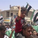 A boy joins demonstrators holding opposition flags as they protest against Syria's President Bashar al-Assad at Binsh near Idlib July 6, 2012. REUTERS/Shaam News Network/Handout
