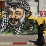 A Palestinian woman walks past a mural depicting late leader Yasser Arafat (R) in Gaza City July 4, 2012. REUTERS/Mohammed Salem