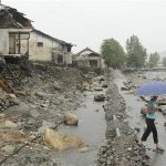 A woman holding an umbrella walks past near damaged houses by recent flooding in Kujang district, in the province of North Pyongan, August 28, 2012. REUTERS/Mission East/Handout