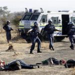 A policeman gestures in front of some of the dead miners after they were shot outside a South African mine in Rustenburg, 100 km (62 miles) northwest of Johannesburg, August 16, 2012. REUTERS/Siphiwe Sibeko