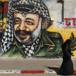 A Palestinian woman walks past a mural depicting late leader Yasser Arafat (R) in Gaza City July 4, 2012. The Palestinian Authority agreed on Wednesday to the exhumation of Arafat's body after new allegations that he was poisoned with the radioactive element polonium-210 in 2004. REUTERS/Mohammed Salem