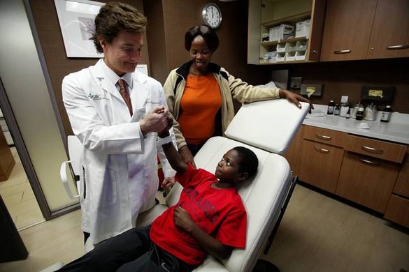 WEST HILLS, CA - DECEMBER 26, 2012: Dr. Peter H. Grossman, left, shacks hands with  Adolf Baguma, 11, of Uganda, while Adolf's guardian Eva Mbabazi, 32, looks on in Dr. Grossman's office in West Hills, CA December 26, 2012. At the age of 5, Adolf was burned by a relative seeking to punish him for taking food. He was left without the ability to walk upright as the skin on the back of his legs fused together. He was abandoned and left in the streets. A Los Angeles attorney met Adolf while on a mission to Uganda. He worked with the Children's Burn Foundation, and Adolf was brought to the Grossman Burn Center, where he underwent a series of corrective surgical procedures to allow him to walk again. (Francine Orr / Los Angeles Times)