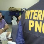 U.S. anti-virus software guru John McAfee (L) sits next to an INTERPOL agent after his detention in Guatemala City December 5, 2012. Guatemalan police arrested McAfee on Wednesday for illegally entering the country and said it would expel him to neighboring Belize, which he fled after being sought for questioning over his neighbor's murder. REUTERS/Policia Nacional Civil/Handout