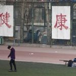 In this Saturday, Jan. 19, 2013 photo. a college student kicks a soccer ball in front of Chinese characters on the fence reading "good health" in Beijing. Despite its formidable performance in recent Olympic Games, China has found itself in a crisis of declining fitness among its youngsters. (AP Photo/Alexander F. Yuan)