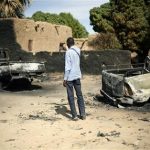 An unidentified man takes a picture of the charred remains of trucks used by radical Islamists on the outskirt of Diabaly, Mali, some 460kms (320 miles) North of the capital Bamako Monday Jan. 21, 2013. French and Malian troops took control Monday of the town of Diabaly, patrolling the streets in armored personnel carriers and inspecting the charred remains of a pickup truck with a mounted machine gun left behind by the fleeing militants. (AP Photo/Jerome Delay)