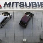 Mitsubishi Motors Corp's vehicles and a passer-by are reflected on an external wall at the company headquarters in Tokyo January 20, 2011. REUTERS/Issei Kato