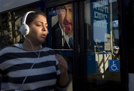 A woman jogs past a vandalized election campaign billboard of Israeli Prime Minister and Likud Party leader Benjamin Netanyahu that is reflected on a bus window in Tel Aviv, Israel, Monday, Jan. 21, 2013.  The general elections will be held on Tuesday, Jan. 22, 2013. (AP Photo/Ariel Schalit)