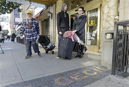 A man, left, leaves the Cecil Hotel with belongings as Michael and Sabina Baugh, both 27, of Plymouth, England, wait for transportation as they leave the hotel in downtown Los Angeles Wednesday, Feb. 20, 2013.  Early Tuesday, police discovered the body of a Canadian woman at the bottom of the historic hotel's water tank, weeks after she was reported missing.  The Baughs, on a 14-day tour package, had been there eight days and had showered in and drank the water. The couple's tour operator was less than cooperative in finding them other accommodations.  (AP Photo/Reed Saxon)