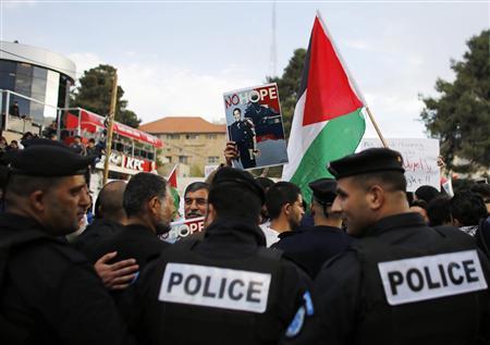 Palestinian policemen stand in front of demonstrators holding digitally manipulated placards depicting U.S President Barack Obama, to prevent them from reaching the main offices of Palestinian President Mahmoud Abbas, during a protest in the West Bank city of Ramallah March 19, 2013. REUTERS/Ammar Awad