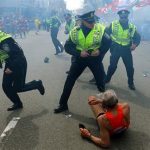 Bill Iffrig, 78, lies on the ground as police officers react to a second explosion at the finish line of the Boston Marathon in Boston, Monday, April 15, 2013. Iffrig, of Lake Stevens, Wash., was running his third Boston Marathon and near the finish line when he was knocked down by one of two bomb blasts. (AP Photo/The Boston Globe, John Tlumacki)