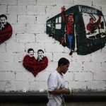 A street artist stands in front of a wall with graffiti showing late Venezuela President Hugo Chavez and current acting President and presidential candidate Nicolas Maduro in Caracas April 10, 2013. Venezuelans will hold presidential elections on April 14. The graffiti (L and C) read, "We are all Chavez." REUTERS/Tomas Bravo