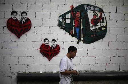 A street artist stands in front of a wall with graffiti showing late Venezuela President Hugo Chavez and current acting President and presidential candidate Nicolas Maduro in Caracas April 10, 2013. Venezuelans will hold presidential elections on April 14. The graffiti (L and C) read, "We are all Chavez." REUTERS/Tomas Bravo