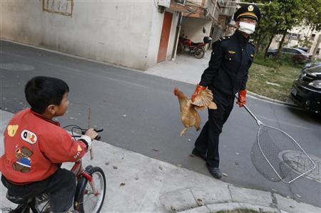 A city management officer holds a chicken as a boy rides past in a residential neighbourhood of Jiaxing, Zhejiang province, April 11, 2013. REUTERS/William Hong