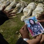 In this photograph taken on Wednesday, May 1, 2013, in Dhaka, Bangladesh, Farida, left, shows a picture of her sister-in-law Fahima to officials as she tries to identify her among the bodies which arrived for burial. Just moments before Fahima was to be placed in one of the dozens of unmarked graves dug for victims of Bangladesh's building collapse, Farida was able to claim and leave with her sister-in-law's body. For Farida and countless other relatives of the garment workers who disappeared when Rana Plaza came crashing down, the past week has been one of tumbling expectations, as hope that their loved ones survived faded into the realization that they may have to return home without even a body to bury. (AP Photo/Ismail Ferdous)