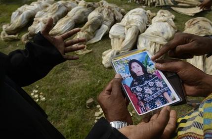 In this photograph taken on Wednesday, May 1, 2013, in Dhaka, Bangladesh, Farida, left, shows a picture of her sister-in-law Fahima to officials as she tries to identify her among the bodies which arrived for burial.  Just moments before Fahima was to be placed in one of the dozens of unmarked graves dug for victims of Bangladesh's building collapse, Farida was able to claim and leave with her sister-in-law's body. For Farida and countless other relatives of the garment workers who disappeared when Rana Plaza came crashing down, the past week has been one of tumbling expectations, as hope that their loved ones survived faded into the realization that they may have to return home without even a body to bury. (AP Photo/Ismail Ferdous)
