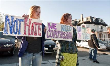 Fiona Gilley, left, and her sister Nairi Melkonian, both of Worcester, Mass., hold signs urging compassion while they stand on the other side of the street from protestors on Sunday evening, May 5, 2013 in Worcester, Mass.  Boston marathon bombing suspect Tamerlan Tsarnaev's body is being held at Graham Putnam & Mahoney Funeral Parlors on Main Street in Worcester, the building at right, until a cemetery can be found that will accept the body for burial. (AP Photo/Worcester Telegram & Gazette, Betty Jenewin)