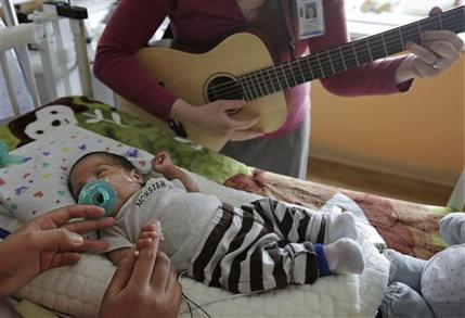Music therapist Elizabeth Klinger, right, quietly plays guitar and sings for Augustin as he grips the hand of his mother, Lucy Morales, in the newborn intensive care unit at Ann & Robert H. Lurie Children's Hospital in Chicago on Monday, May 6, 2013. Research suggests that music may help those born way too soon adapt to life outside the womb. Recent studies and anecdotal reports suggest the vibrations and soothing rhythms of music, especially performed live in the hospital, might benefit preemies and other sick babies. (AP Photo/M. Spencer Green)