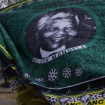 A woman walks behind a fabric bearing a portrait of former president Nelson Mandela in Soweto, South Africa Sunday June 9, 2013. Mandela has been hospitalized with an occurring lung infection. The latest government report says that he remains in a serious but stable condition. (AP Photo/Denis Farrell)