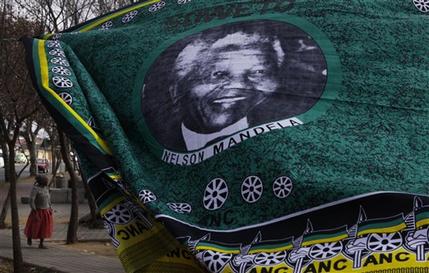 A woman walks behind a fabric bearing a portrait of former president Nelson Mandela in Soweto, South Africa   Sunday June 9, 2013. Mandela has been hospitalized with an occurring lung infection. The latest government report says that he remains in a serious but stable condition. (AP Photo/Denis Farrell)