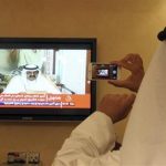 A man prepares to take a picture with his mobile photo of a televised address by Qatar's Emir Sheik Hamad bin Khalifa Al Thani, in Doha, Qatar,Tuesday, June 25, 2013. Qatar's ruler said Tuesday he has transferred power to the 33-year-old crown prince in an anticipated move that puts a new generation in charge of the Gulf nation's vast energy wealth and rising political influence. (AP Photo/Osama Faisal)