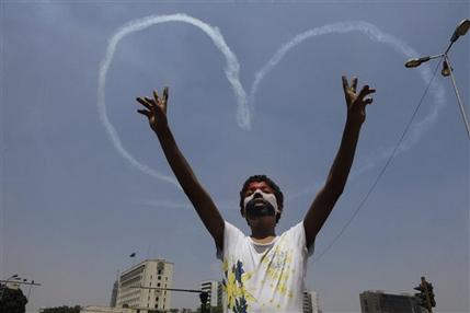 An Egyptian protester flashes v signs for military aircrafts forming a heart shape trails in the sky over Tahrir Square in Cairo, Egypt, Friday, July 5, 2013. Egypt's Muslim Brotherhood called for a wave of protests Friday, furious over the military's ouster of its president and arrest of its revered leader and other top figures, underlining the touchy issue of what role the fundamentalist Islamist movement might play in the new regime. (AP Photo/Amr Nabil)