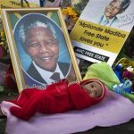 Oamohetswe Mabitsela, 4 months old, is placed by his mother next to a picture of Nelson Mandela for her to take a photograph of him with her camera phone, outside the Mediclinic Heart Hospital where former South African President Nelson Mandela is being treated in Pretoria, South Africa Thursday, July 4, 2013. The remains of Nelson Mandela's three deceased children were reburied at their original resting site on Thursday, a day after a court ordered their return two years after Mandela's grandson moved the bodies. (AP Photo/Ben Curtis)