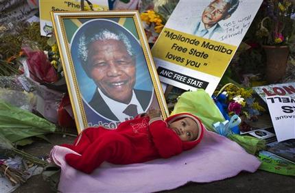 Oamohetswe Mabitsela, 4 months old, is placed by his mother next to a picture of Nelson Mandela for her to take a photograph of him with her camera phone, outside the Mediclinic Heart Hospital where former South African President Nelson Mandela is being treated in Pretoria, South Africa Thursday, July 4, 2013. The remains of Nelson Mandela's three deceased children were reburied at their original resting site on Thursday, a day after a court ordered their return two years after Mandela's grandson moved the bodies. (AP Photo/Ben Curtis)