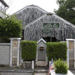 The beer can house, a Houston landmark, sits between newer homes Wednesday, July 10, 2013, in Houston. Former owner John Milkovisch covered the outside on the house with siding made of cut and flatten beer cans and garlands made from the lids. The Orange Show Center for Visionary Art, a local nonprofit that preserves art installations in the city, bought the property about 10 years ago, restored the house and it opened it to the public. (AP Photo/Pat Sullivan)