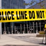 Crime scene tape with a camerman in the near background and a SWAT team in the far background.