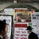 In this Sunday, July 14, 2013 photo, ultra-Orthodox Jewish men walk past a poster in the ultra-Orthodox Jewish Mea Shearim neighborhood in Jerusalem. A large cartoon poster depicts Haredi soldiers rolling through the streets atop tanks trying to lure young boys onto their vehicles. The ad denounces the soldiers as Zionist "ambassadors" and "missionaries." The soldiers in sidecurls have been coined the insulting nickname "Hardak" _ a combination of Haredi and insect. (AP Photo/Sebastian Scheiner)