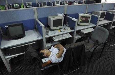 An investor sleeps on chairs next to a computer screen showing stock information at a brokerage house in Hefei