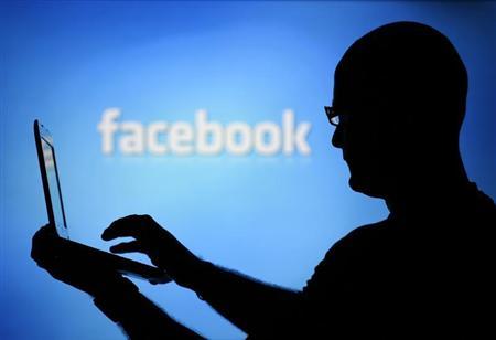 A man is silhouetted against a video screen with an Facebook logo as he poses with an Dell laptop in this photo illustration taken in the central Bosnian town of Zenica