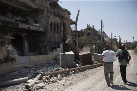 Free Syrian Army fighters walk past damaged buildings and debris in Deir al-Zor