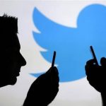 Men are silhouetted against a video screen with an Twitter logo as he poses with an Samsung S4 smartphone in this photo illustration taken in the central Bosnian town of Zenica
