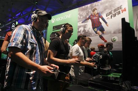 Visitors play "FIFA 14" with the Xbox One at the Microsoft Games exhibition stand during the Gamescom 2013 fair in Cologne