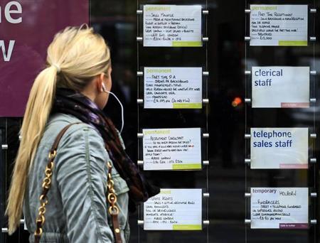 A woman passes notices for jobs in the window of a recruitment agency in London
