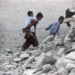 Survivors of an earthquake walk on rubble of a mud house after it collapsed following the quake in the town of Awaran