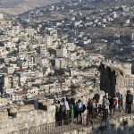 Arab neighbourhoods in East Jerusalem are seen in the background as tourists walk atop a wall surrounding Jerusalem's Old City
