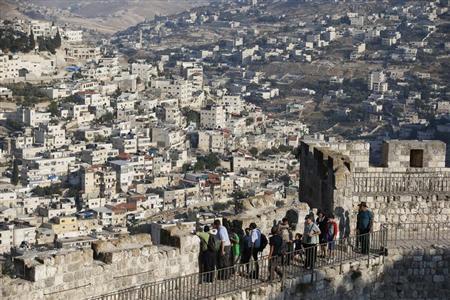 Arab neighbourhoods in East Jerusalem are seen in the background as tourists walk atop a wall surrounding Jerusalem's Old City
