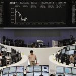 Traders are pictured at their desks in front of the DAX board at the Frankfurt stock exchange