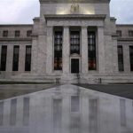 The facade of the U.S. Federal Reserve building is reflected on wet marble during the early morning hours in Washington