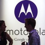 A man and woman laugh in front of a Motorola logo at a launch event for Motorola's new Moto X phone in New York