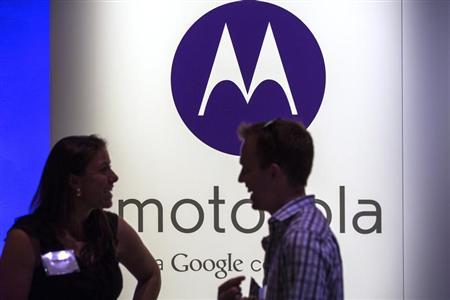 A man and woman laugh in front of a Motorola logo at a launch event for Motorola's new Moto X phone in New York