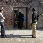 A policeman stands guard as female polio workers wait to give polio vaccine drops to children in Lahore