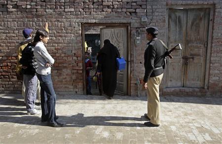 A policeman stands guard as female polio workers wait to give polio vaccine drops to children in Lahore