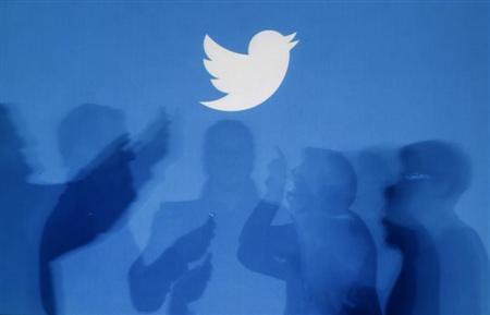 Shadows of people holding mobile phones are cast onto a backdrop projected with the Twitter logo in Warsaw